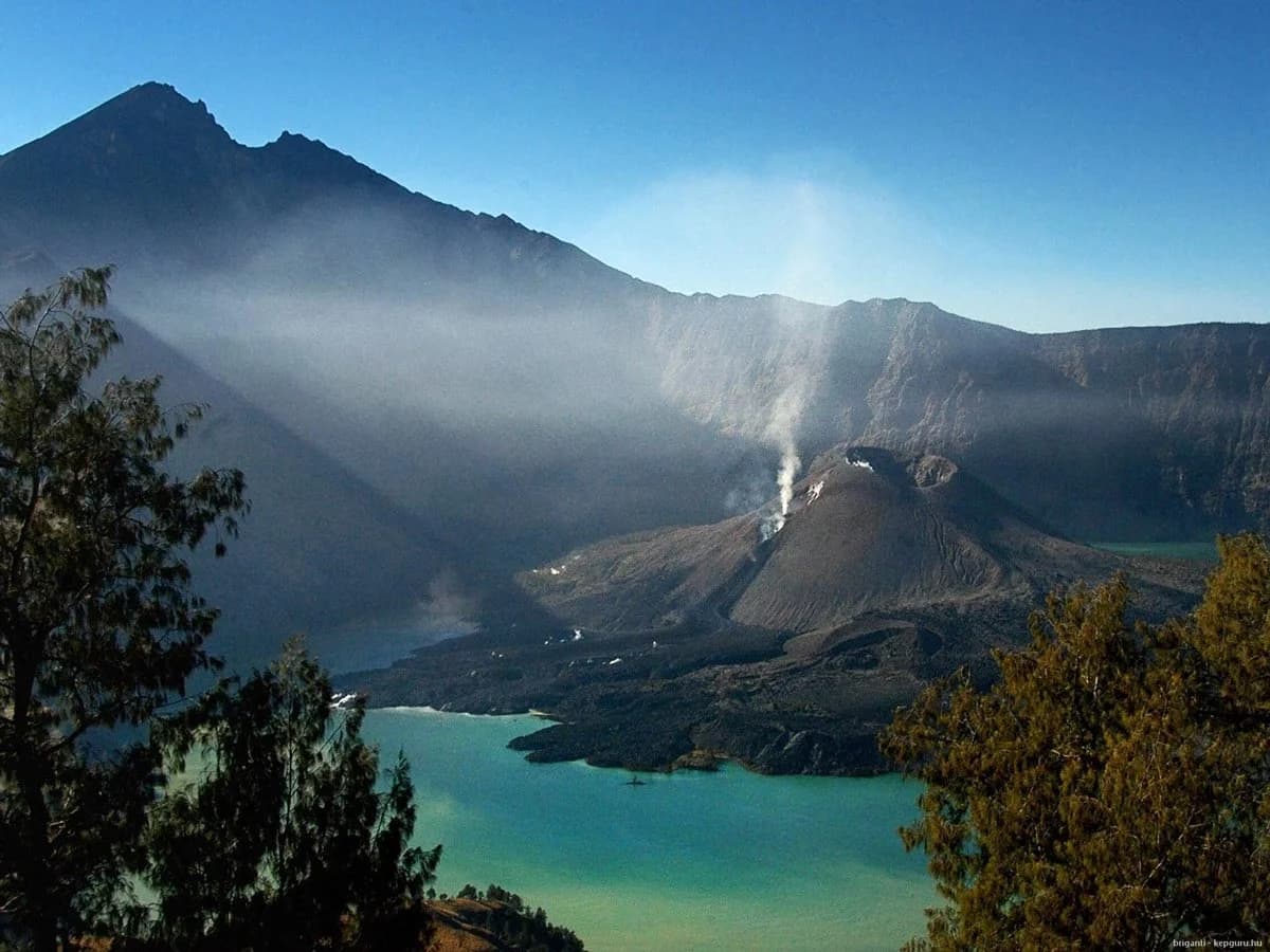 Vibrant turquoise waters of Mount Batur, Bali, framed by lush hills and misty mountains, perfect for guided tours.