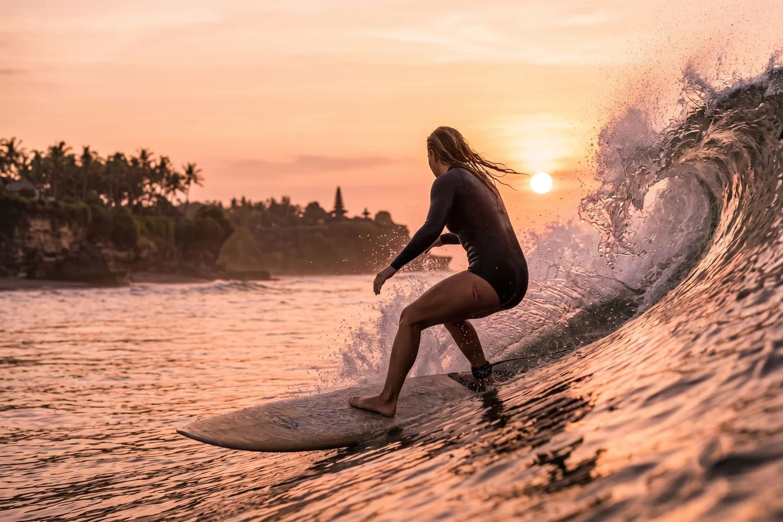 A surfer riding a wave off the coast of Bali at sunset