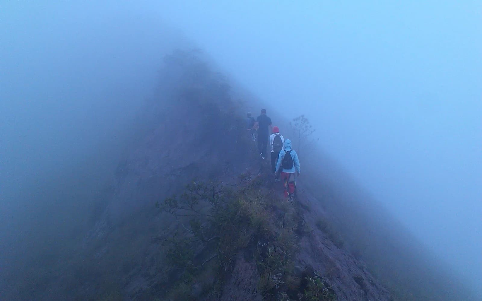 Hikers in rain gear trek a rocky ridge at night during a Mount Batur tour in Bali.