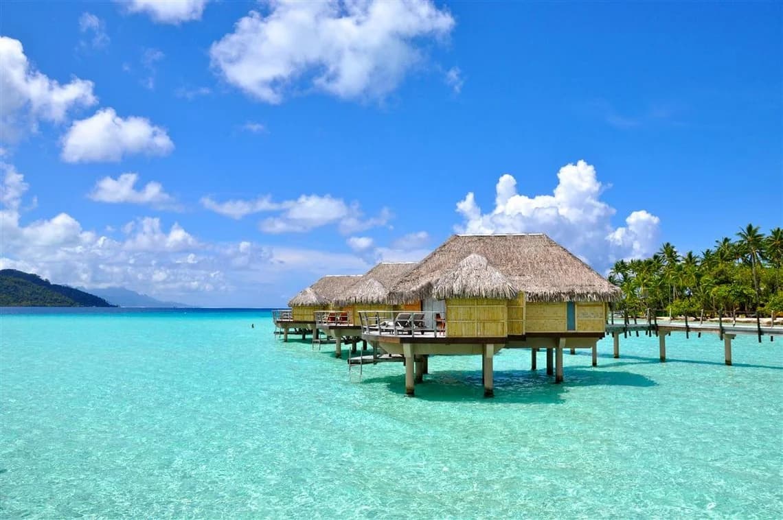 Красивые водные бунгало на острове Gili Trawangan над бирюзовой водой, окружённые зелеными холмами. Острова Гили.